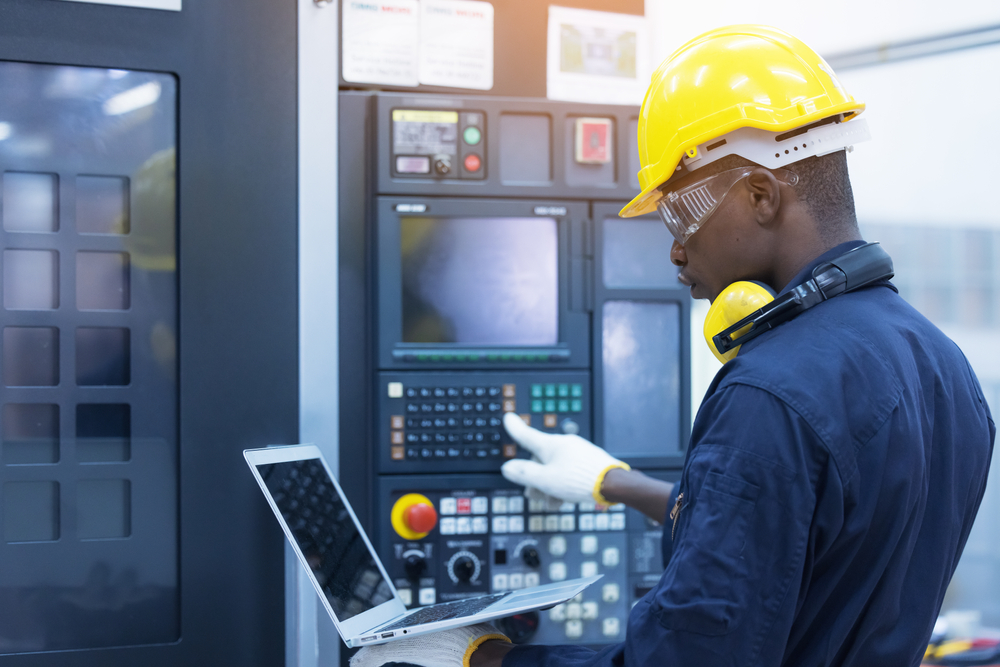 A person holding a laptop computer in one hand interacts with the HMI of a CNC controller with the other hand.